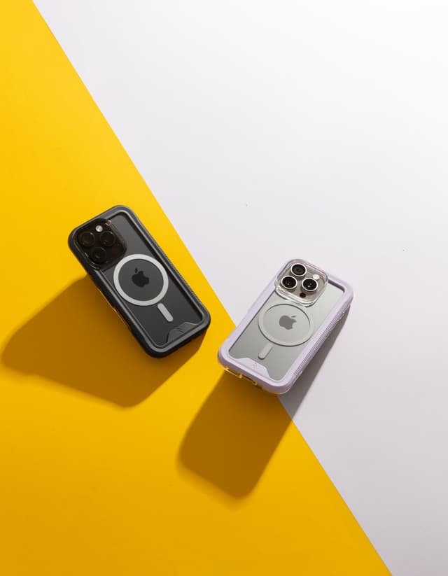 A black-bumper ZIZO ION MagSafe case on a yellow ground beside a purple-bumper one on white, split by a hard diagonal, both casting long shadows