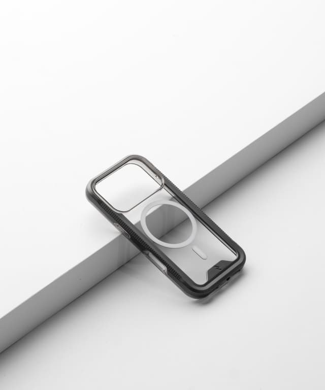 An empty ZIZO ION MagSafe shell with a smoke bumper resting on a pale riser, showing the camera cutout, the textured side rail and the magnet ring with no phone inside