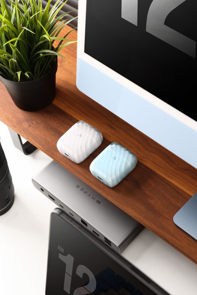 Two ZIZO Halos charging cases on a wooden desk shelf beside a monitor and a laptop