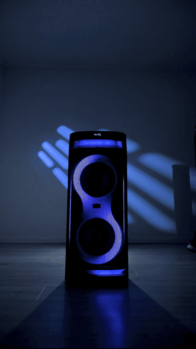 The ZIZO Boom tower speaker standing alone on a dark floor, both driver rings and the top deck lit blue