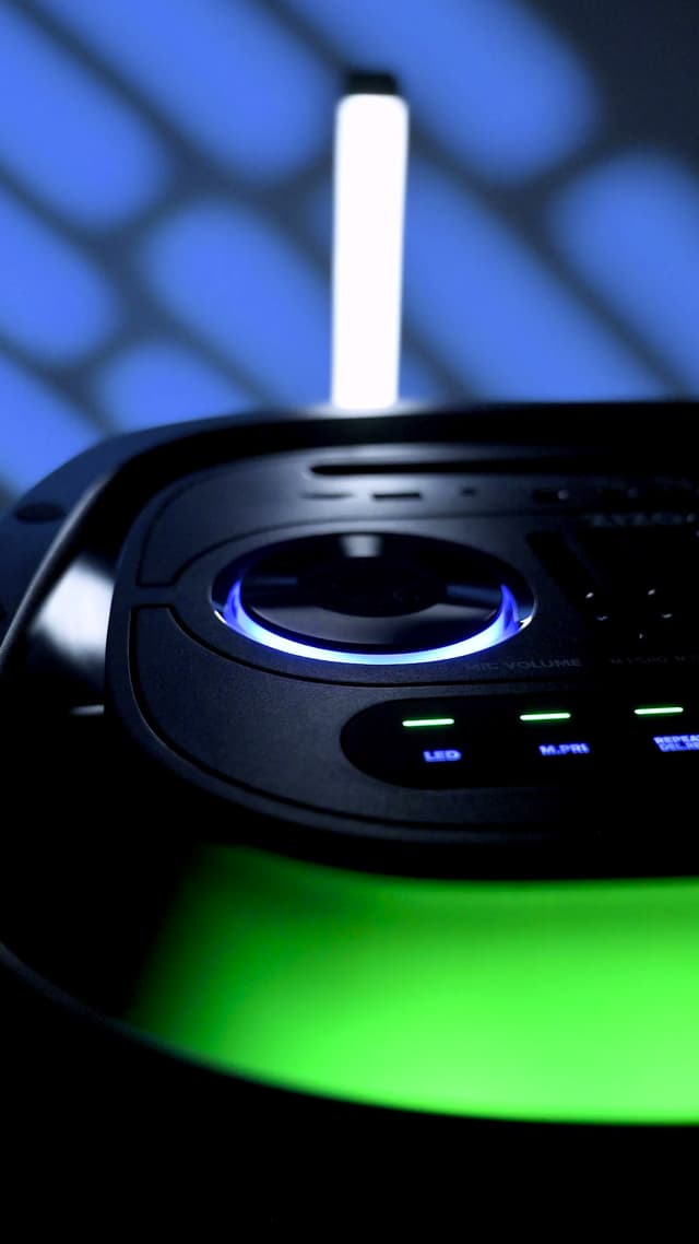 The ZIZO Boom speaker's control panel glowing blue and green in a dark room, a jog wheel and buttons lit
