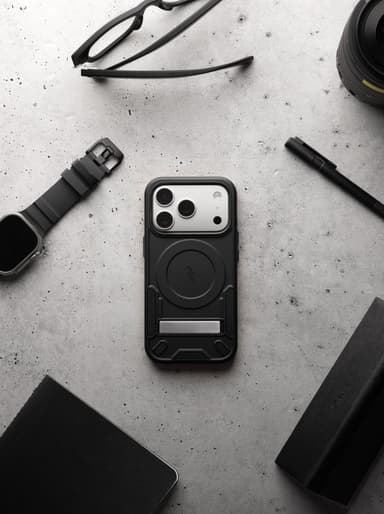 A black ZIZO Transform case on an iPhone Pro staged among glasses, a smartwatch, a pen, a notebook and a camera lens on concrete