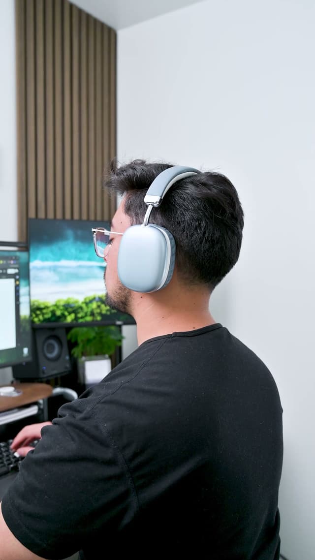 A person working at a desk in pale ZIZO Tempo Pro headphones, a monitor and a wood slat wall behind them