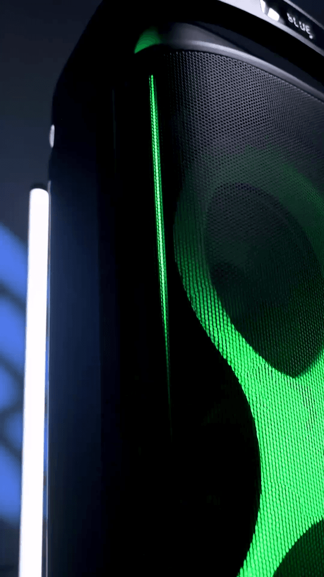 The side of the ZIZO Boom tower speaker, a green light seam running its full height and a driver ring glowing through the grille mesh