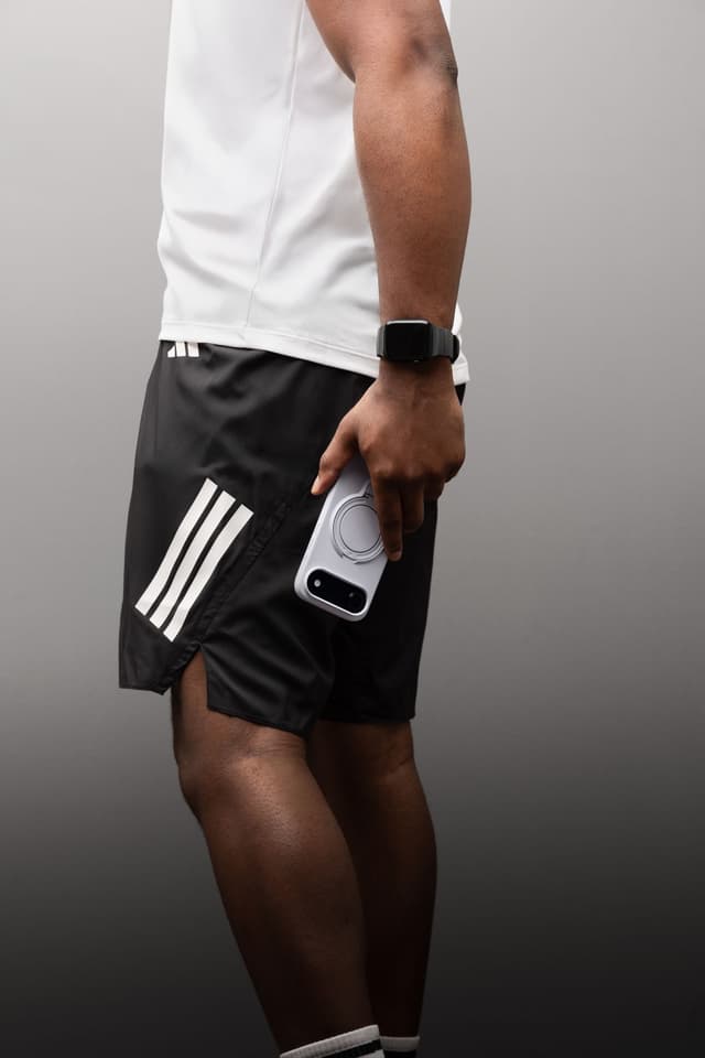 A person in a white athletic top holding a frosted-white ZIZO Revolve case loosely at hip height, the ring grip visible in hand