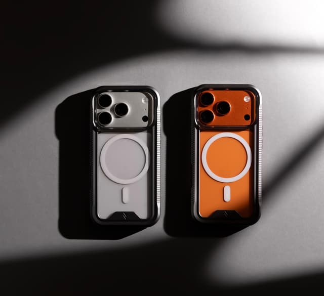 Two ZIZO ION MagSafe cases with black bumpers and clear backs on a silver iPhone 17 Pro and a cosmic orange iPhone 17 Pro, side by side under hard directional light, each phone's own finish reading through the clear back