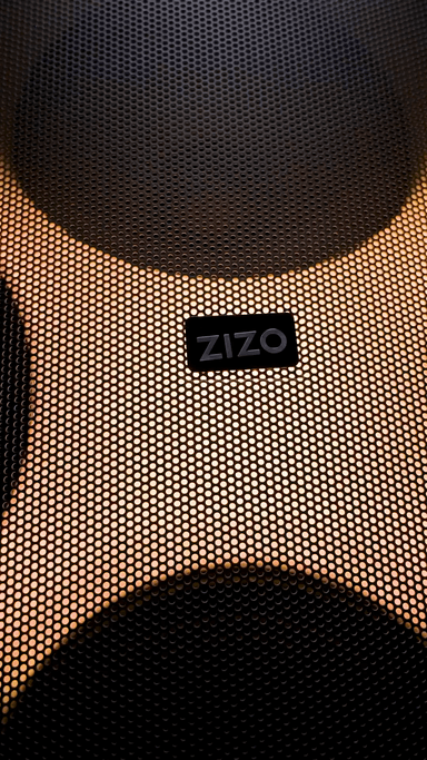 The ZIZO Boom speaker's perforated grille lit amber, the ZIZO badge on the mesh and a driver ring glowing behind it