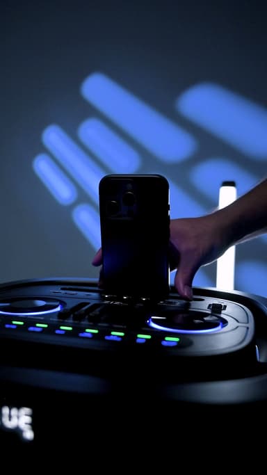 Hands placing a phone into the dock on top of the ZIZO Boom party speaker under blue lighting