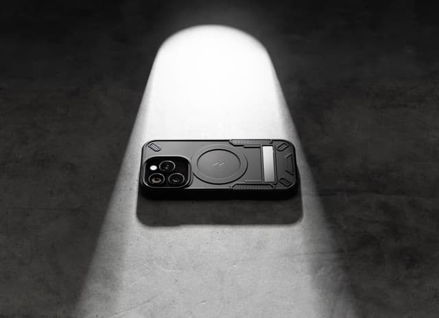 A black ZIZO Transform case isolated by a single hard spotlight on raw concrete, its sliding camera cover and textured grip panels catching the light