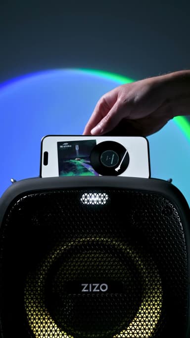The ZIZO Tune Z3 black party speaker with a phone resting in the dock on top, one large driver ring lit against a blue and green gradient backdrop