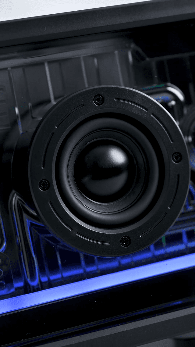 The woofer and tweeter of the ZIZO Retro Crystal speaker seen through its transparent black shell, lit blue by the RGB bar below