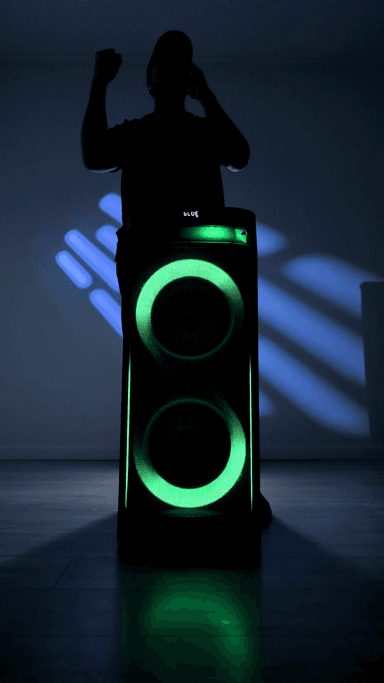 The ZIZO Boom tower speaker in a dark room, its two driver rings and front panel cycling through green and blue while a person dances behind it