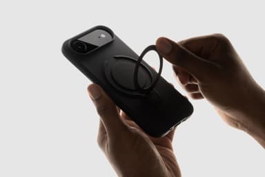 Backlit hands attaching a magnetic ring stand to the back of a black ZIZO Revolve case on an iPhone