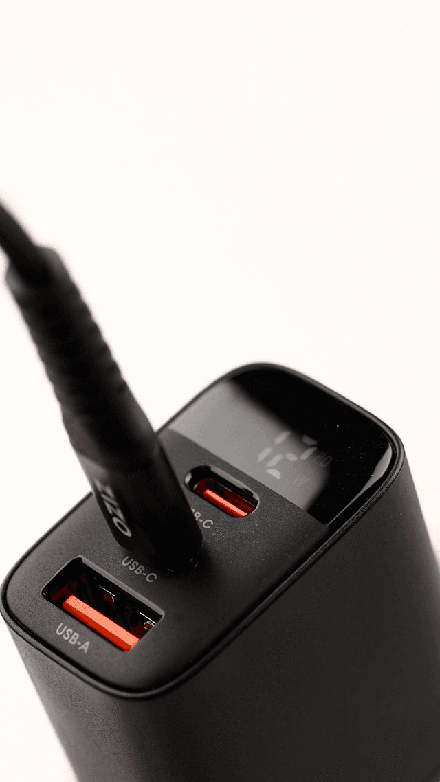 Macro shot of a ZIZO PowerVault power bank's USB-C and USB-A ports with a digital wattage display and a braided black ZIZO cable plugged in