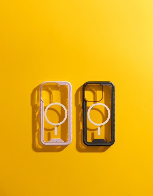Two empty ZIZO ION MagSafe cases lying on a bright yellow surface, one with a purple bumper and one with a black bumper, each showing its clear back and a white magnet ring at the center