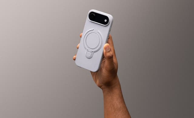 A raised hand showing the sculpted ring stand on the back of a lavender-gray ZIZO Revolve case, against a moody gray backdrop