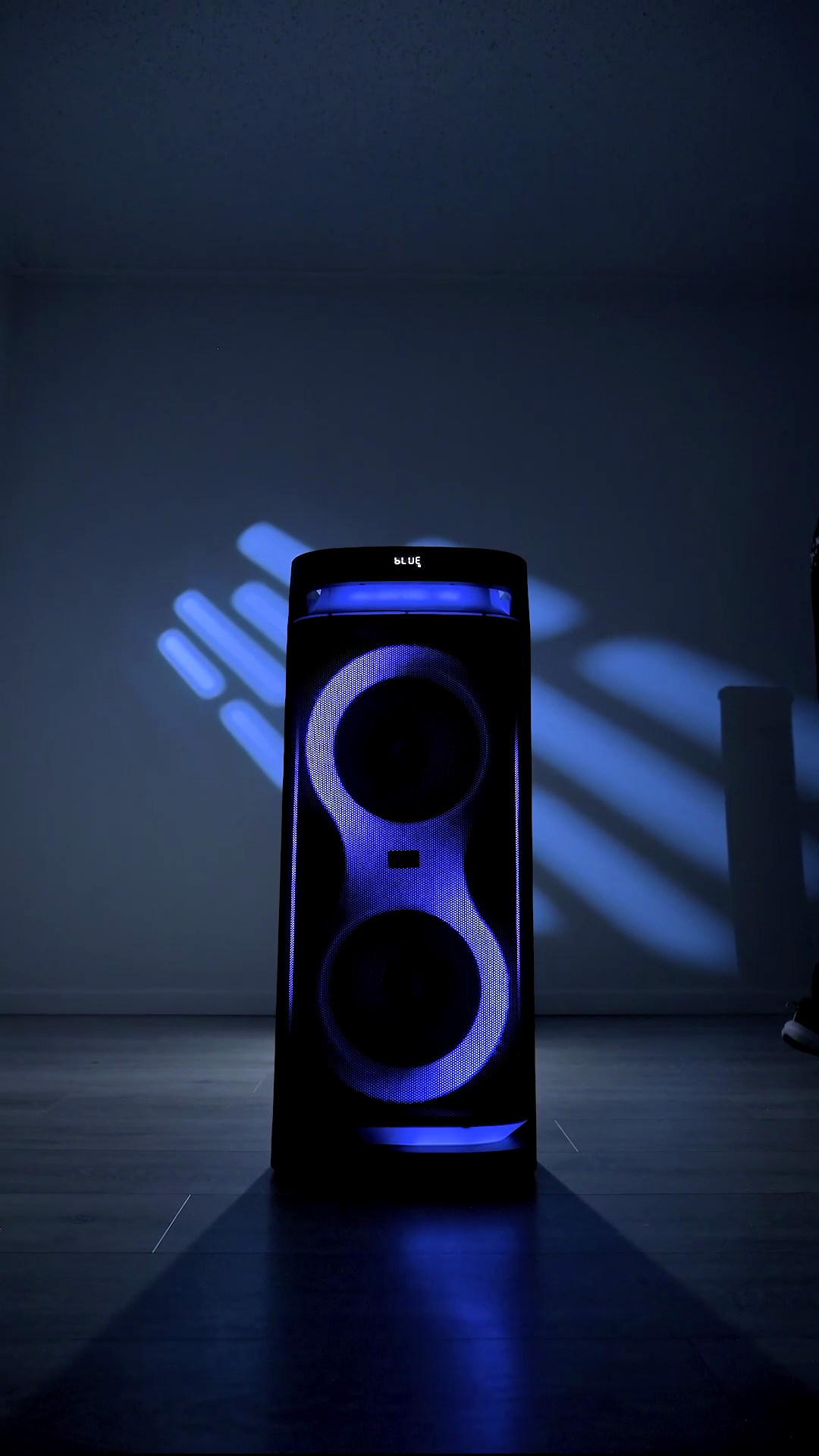 The ZIZO Boom tower speaker standing alone on a dark floor, both driver rings and the top deck lit blue
