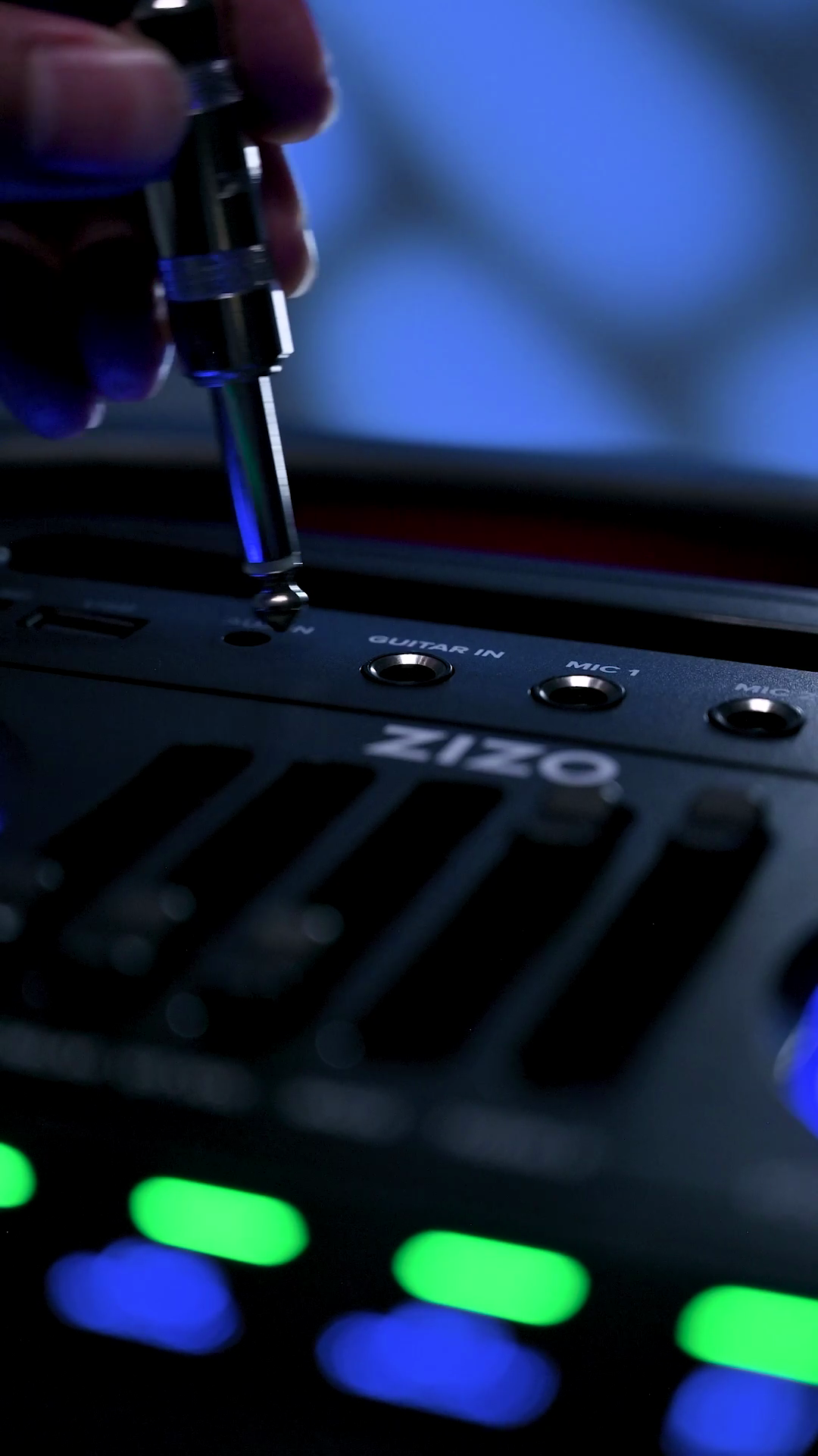 A hand plugging a jack into the microphone input on the ZIZO Boom speaker's top deck, beside the lit function pads