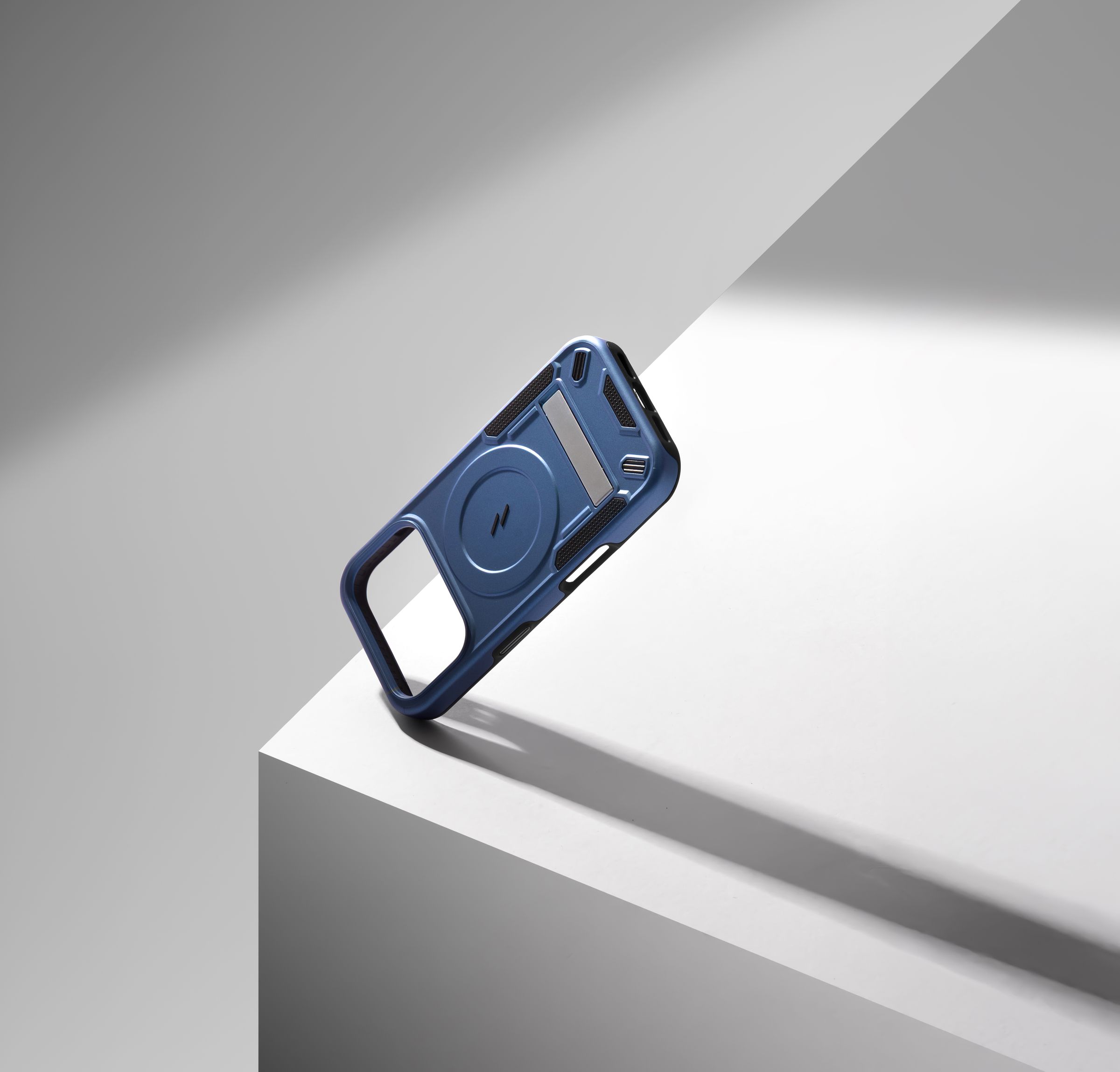 An empty blue ZIZO Transform case teetering on the edge of a white geometric block, a hard diagonal shadow across the frame