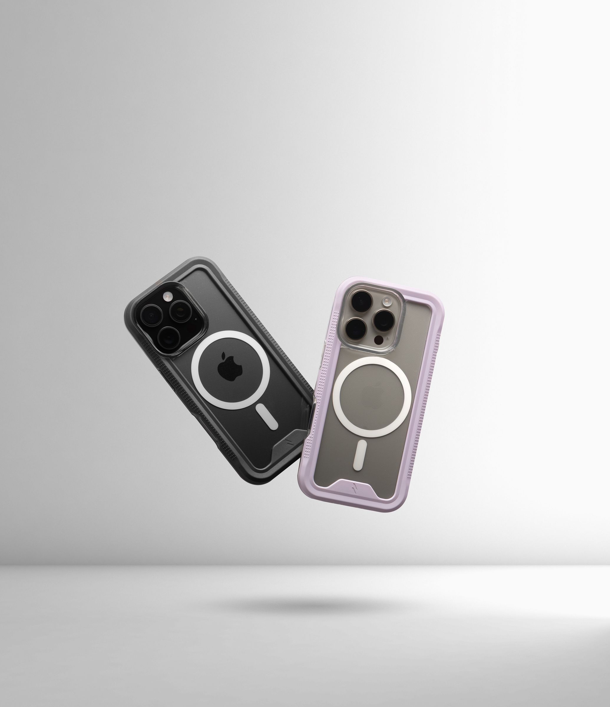 A black-bumper and a purple-bumper ZIZO ION MagSafe case floating mid-air against a soft gray gradient, both clear backs and white magnet rings facing the camera