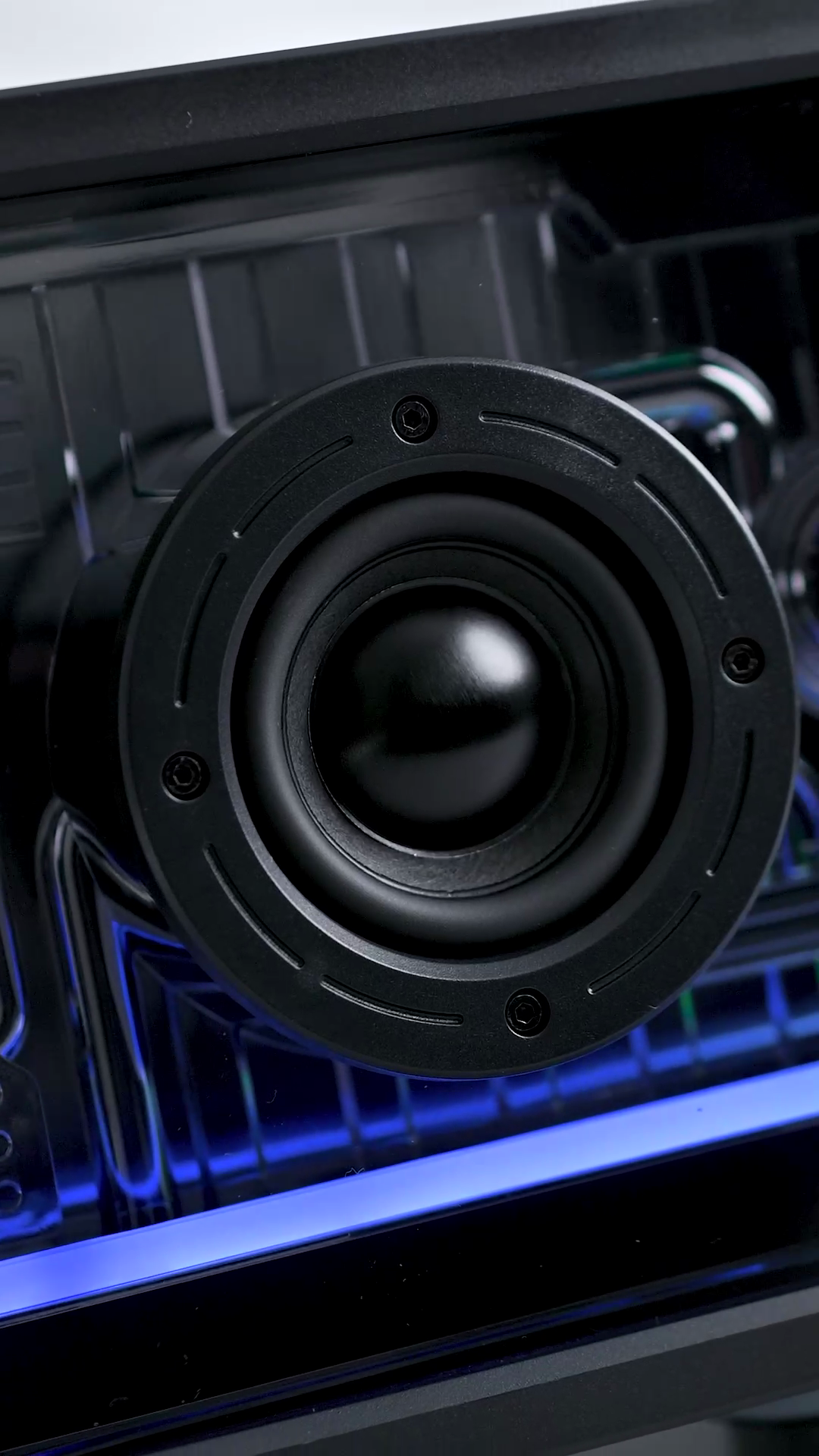 The woofer and tweeter of the ZIZO Retro Crystal speaker seen through its transparent black shell, lit blue by the RGB bar below