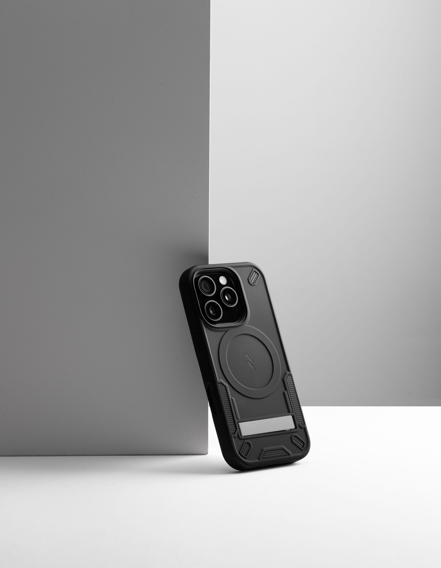A black ZIZO Transform case on a phone tipped against a two-tone gray studio backdrop, a crisp shadow line across the matte shell
