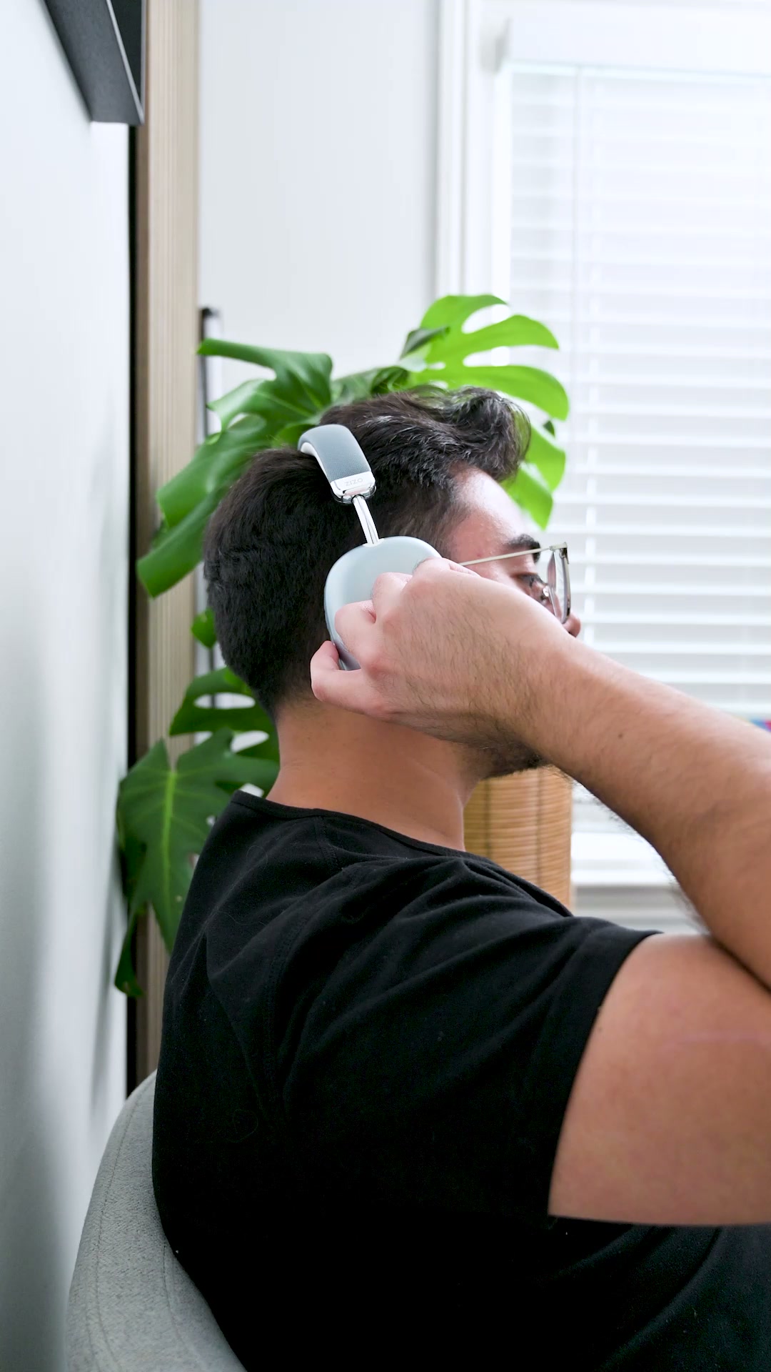 A person beside a window resting a hand on the earcup of the pale ZIZO Tempo Pro headphones they are wearing