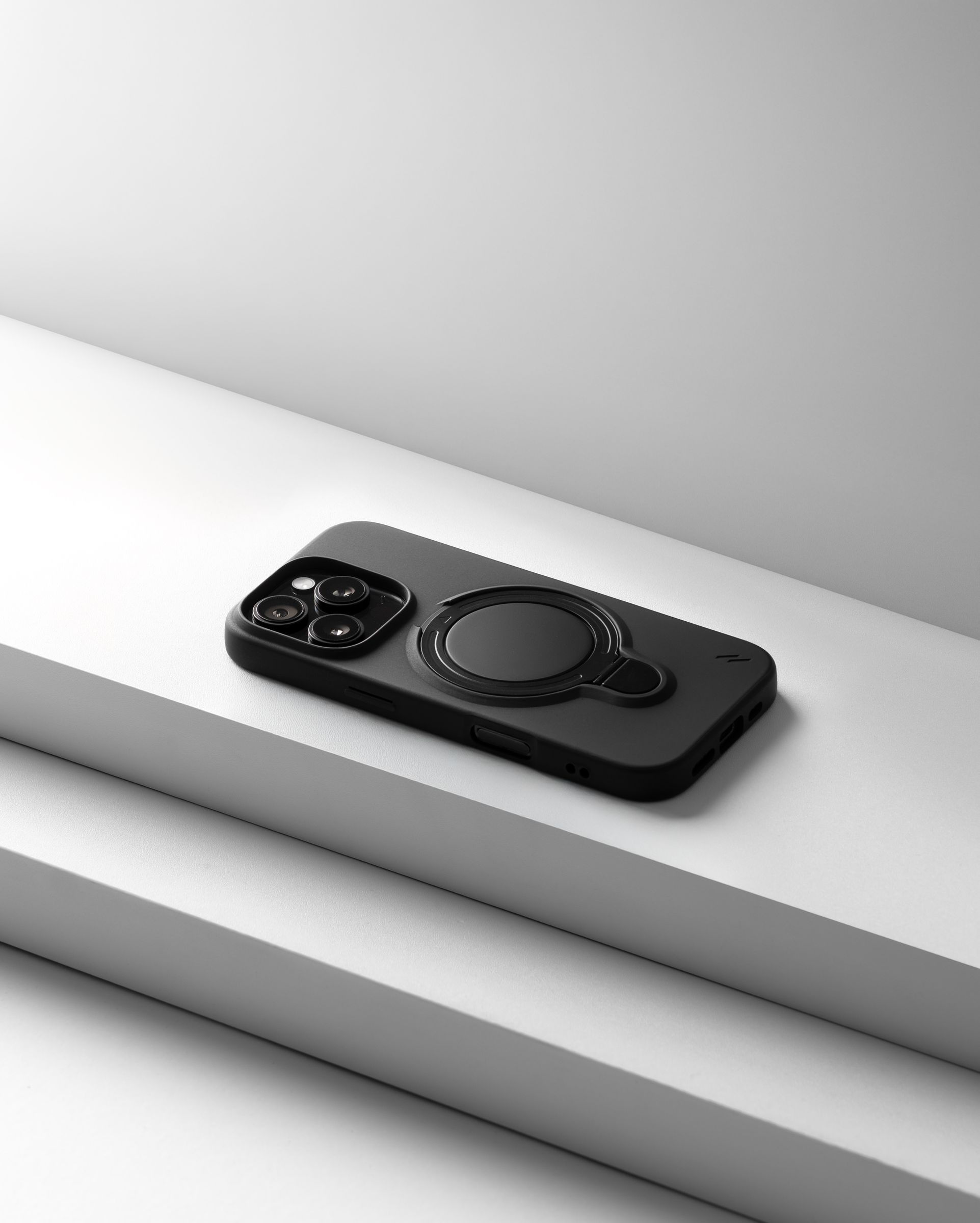 A matte black ZIZO Revolve case on an iPhone, resting on stair-stepped studio blocks in soft directional light