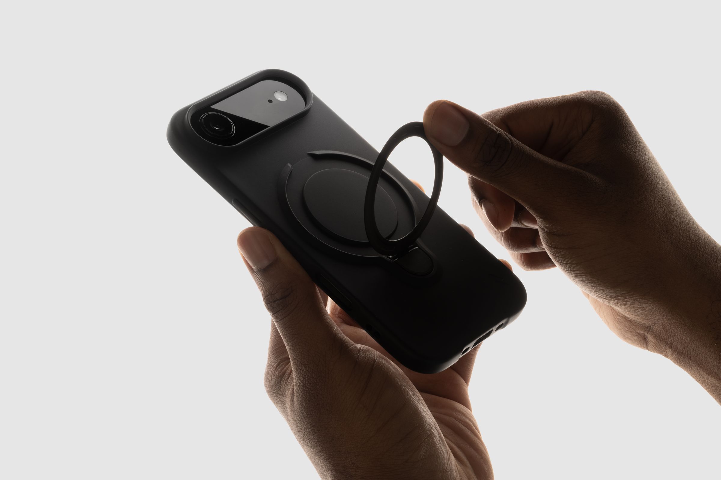 Backlit hands attaching a magnetic ring stand to the back of a black ZIZO Revolve case on an iPhone