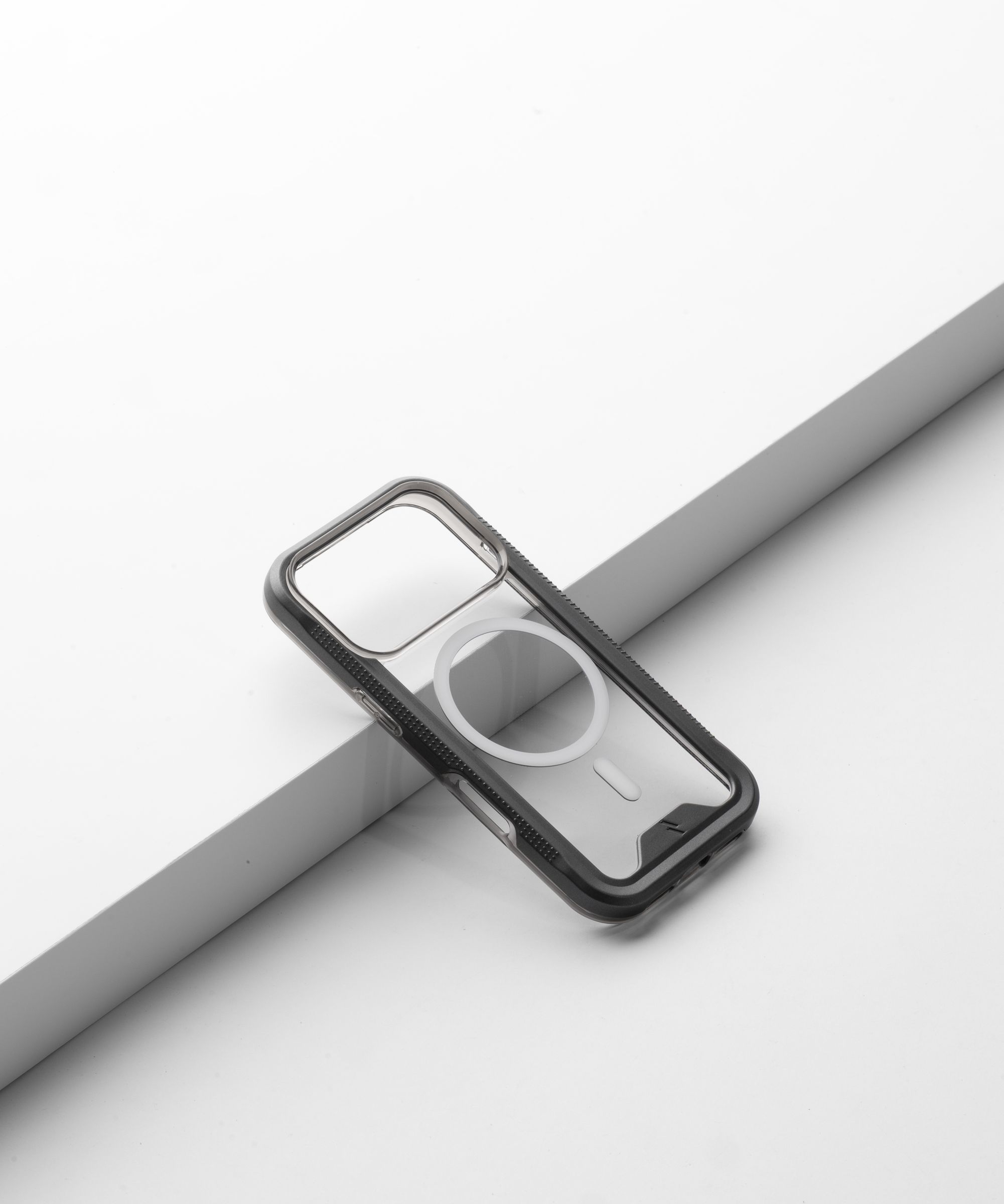An empty ZIZO ION MagSafe shell with a smoke bumper resting on a pale riser, showing the camera cutout, the textured side rail and the magnet ring with no phone inside