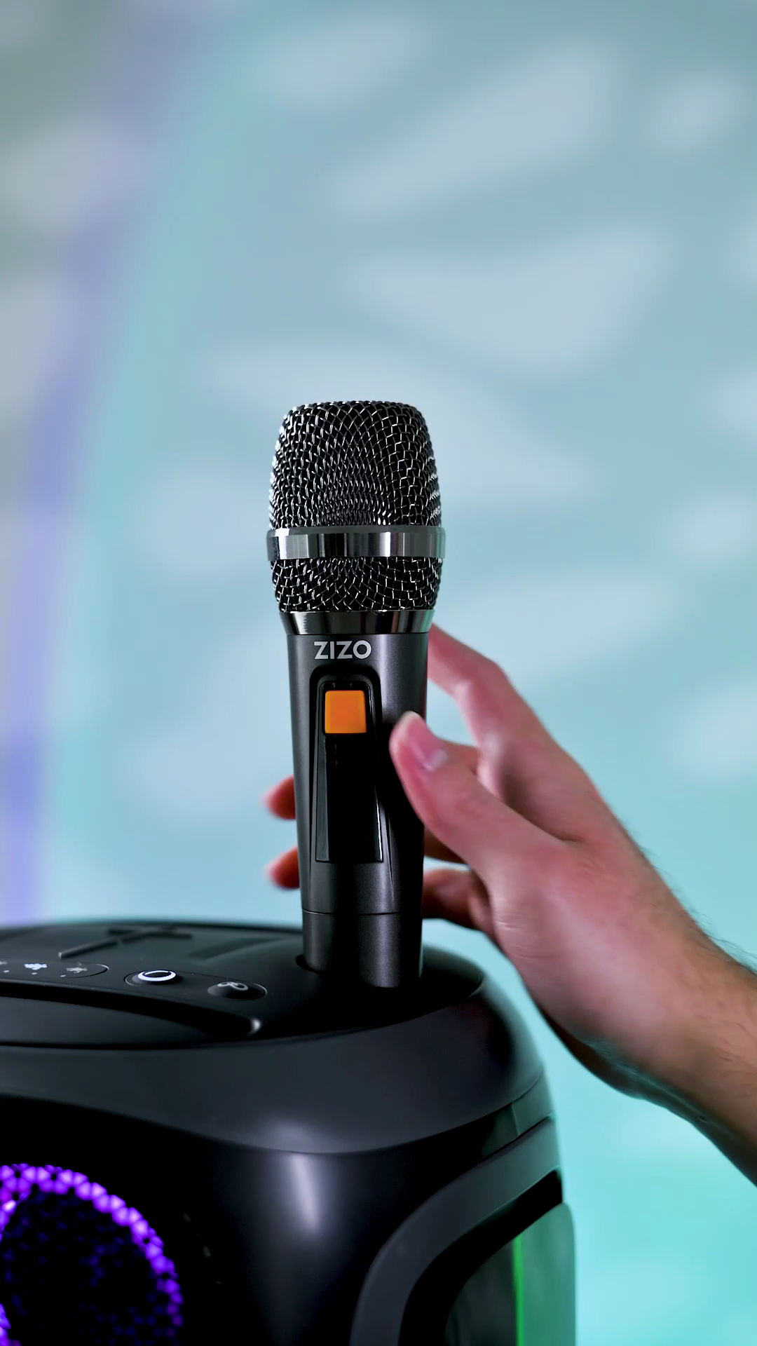 A hand lifting one of the ZIZO Tune Z5's two wireless microphones out of its cradle on the speaker's top panel